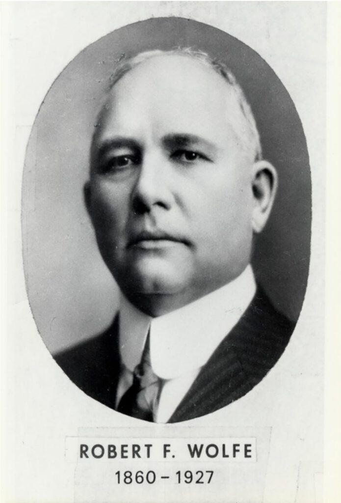 Black and white portrait of a man in a suit and tie, facing forward. Below the photo, text reads: Robert F. Wolfe 1860 – 1927.