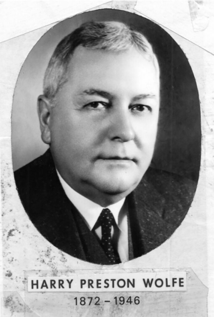 Black-and-white portrait of an older man in a suit and tie, with short gray hair. Below the oval photo is the name Harry Preston Wolfe and the years 1872–1946.
